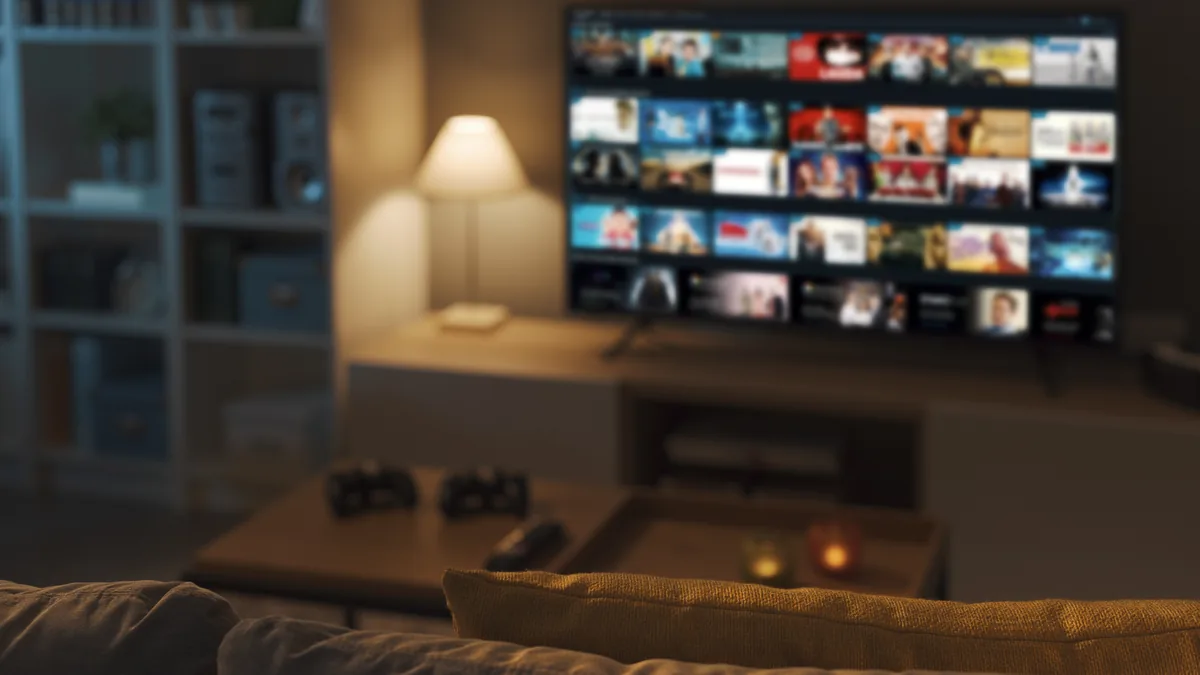 Mørk stue der en stor TV med rutenett av programbilder lyser opp sofa og stuebord