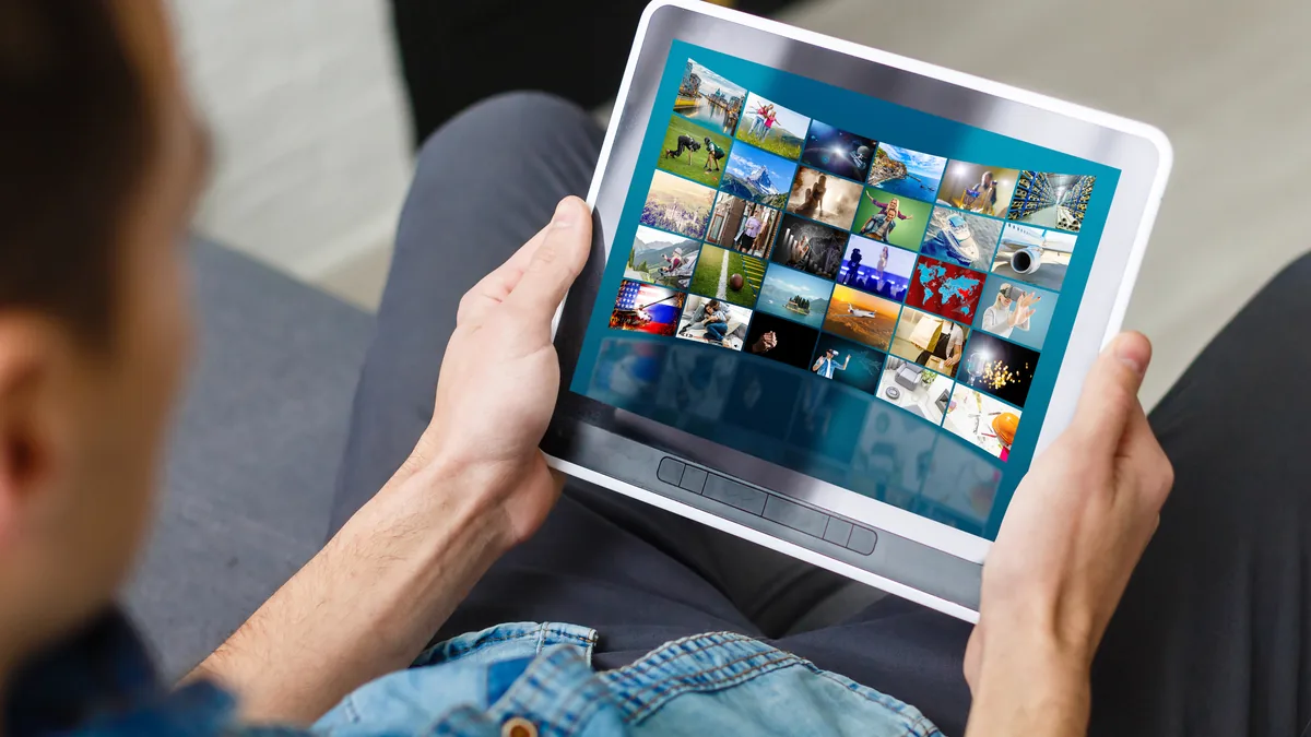 Mann i olabluse holder et nettbrett som viser et rutenett av videominiatyrer