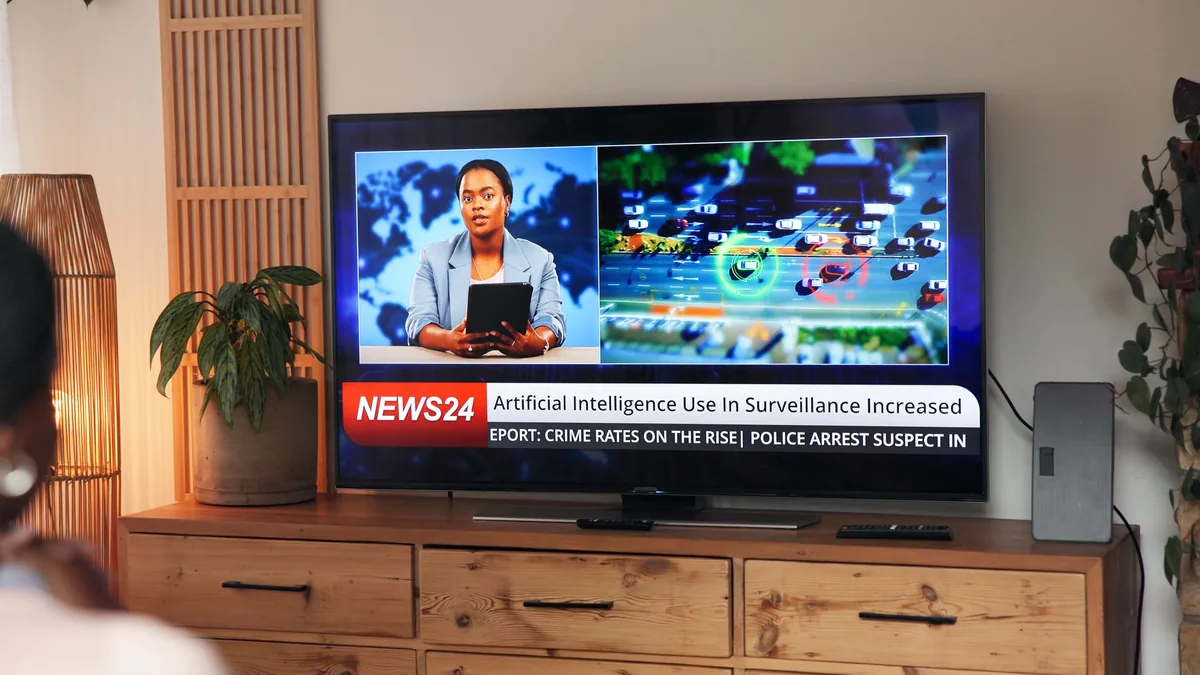 Flatskjerm-TV på en trekommode viser en nyhetssending med programleder og nyhetsstripe