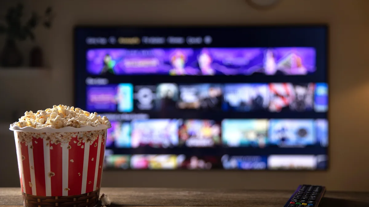 Stripete popcornbeger og fjernkontroll på et trebord foran en TV som viser en strømmemeny