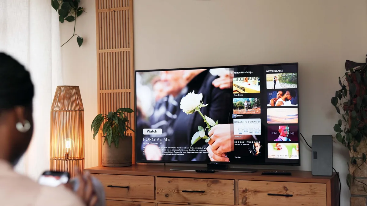 Kvinne med fjernkontroll ser på en TV som viser et filmutvalg med plakater og kategorier