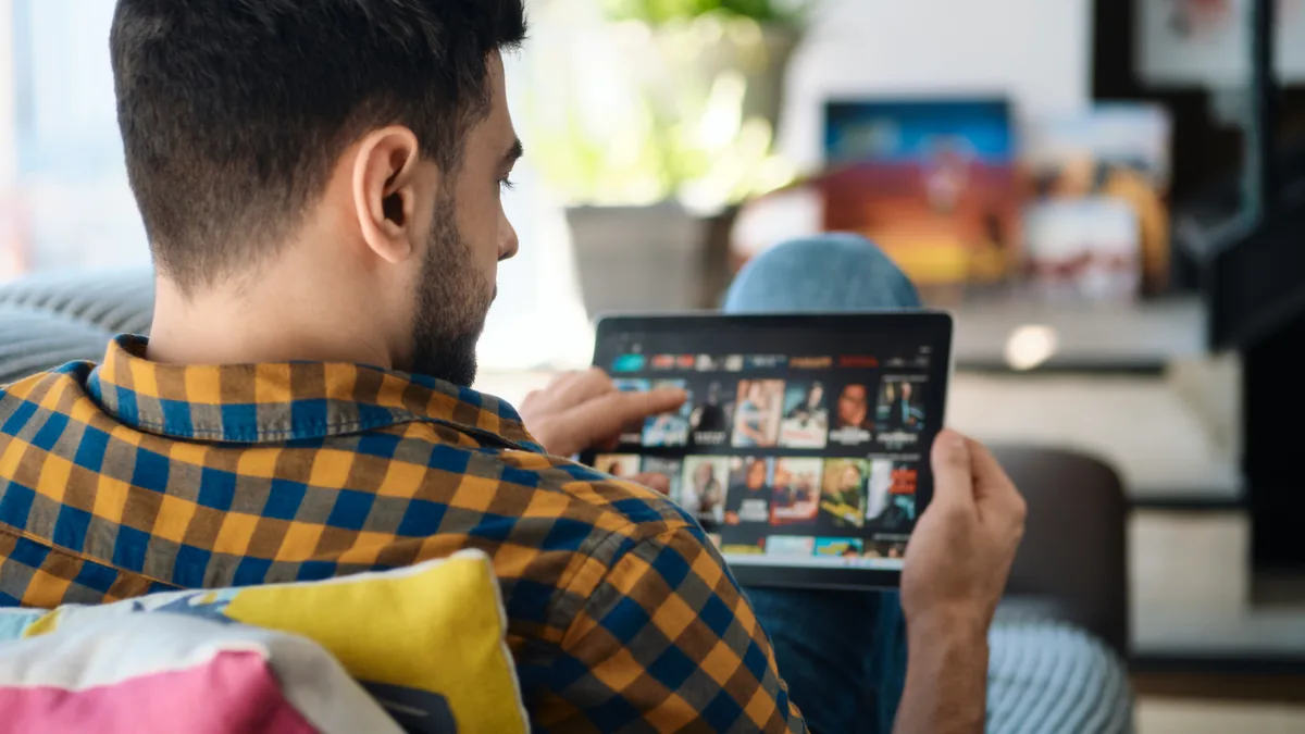 Mann i rutete skjorte trykker på et nettbrett som viser en app med filmplakater